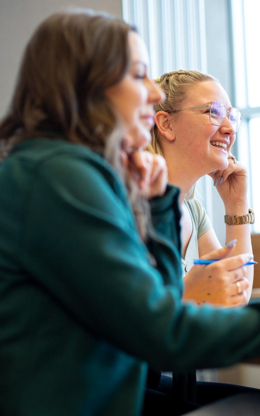 Two students are sitting in a classroom, looking off into the distance and smiling